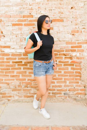 Téléchargez les photos : Femme hispanique élégante posant pour une maquette de t-shirt devant un mur de briques rustique, parfaite pour mettre en valeur la mode et les dessins de vêtements - en image libre de droit