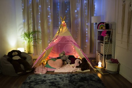 Foto de Encantador cambio de imagen dormitorio crea un caprichoso campamento nocturno para una niña, completo con luces de hadas y juguetes de peluche - Imagen libre de derechos