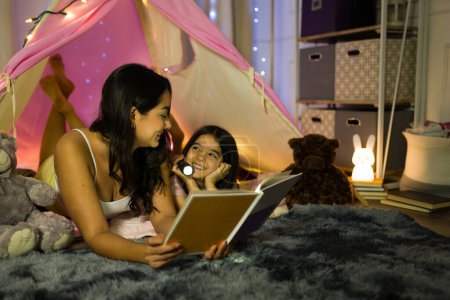 Téléchargez les photos : Maman et enfant profitent d'une histoire au coucher dans un cadre confortable à la maison la nuit, créant des souvenirs chéris dans leur chambre chaude - en image libre de droit