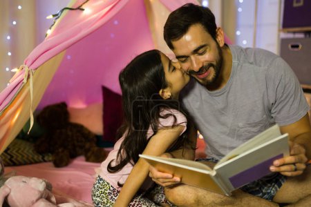 Father and daughter bonding over a bedtime story inside a cozy tent, creating a special moment of love and getting a kiss on the cheek