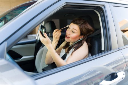 Foto de Multitareas enfocadas a la mujer, aplicación de maquillaje con un cepillo en un coche, ejemplificando la prisa de la vida moderna y desafiando las normas de conducción seguras - Imagen libre de derechos