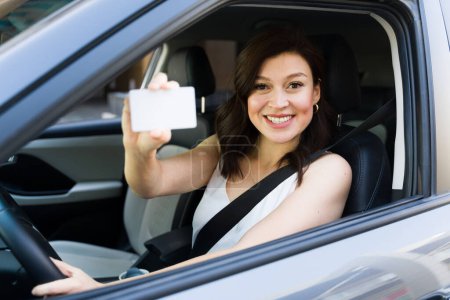 Téléchargez les photos : Joyeuse conductrice présentant son permis de conduire alors qu'elle était assise dans sa voiture, exsudant confiance et positivité sur la route - en image libre de droit