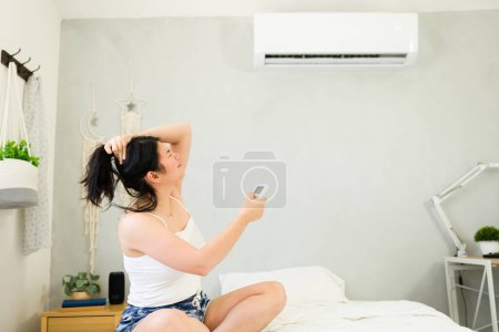 Téléchargez les photos : Woman relaxing on her bed, enjoying the refreshing breeze from a mini split ac unit on a hot summer day - en image libre de droit