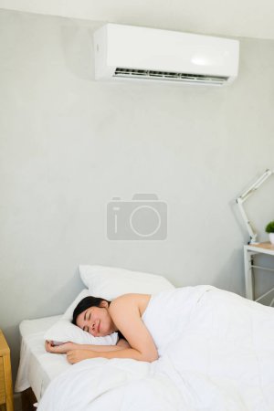 Téléchargez les photos : Caucasian woman peacefully relaxes in bed, savoring the refreshing relief of a modern mini split air conditioning unit on a hot summer day - en image libre de droit