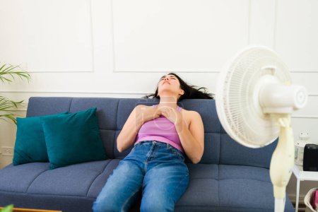 Woman trying to cool off in her home during the hot summer with the help of a fan, expressing discomfort from heat