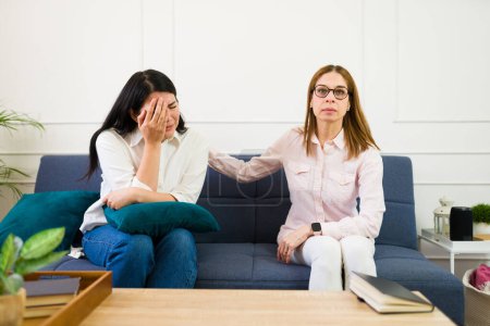 Experienced female psychologist offers comforting support to a tearful patient in a calming therapy setting, emphasizing emotional wellness and mental health assistance