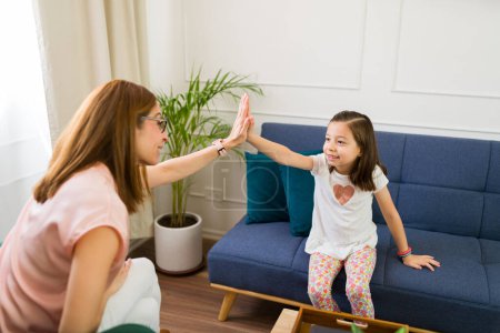 Photo for Compassionate child psychologist gives a high-five to a smiling little girl during a positive therapy session in a bright, welcoming room - Royalty Free Image