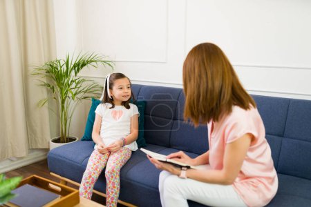 Photo for Professional child psychologist sits attentively with a clipboard during a therapy session with a little girl in a peaceful office setting - Royalty Free Image