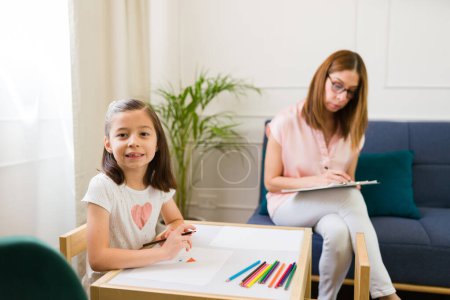 Photo for Portrait of a pretty Caucasian girl doing a drawing as part of an art therapy session with a child psychologist - Royalty Free Image