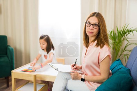 Professional child psychologist making eye contact while working with a little girl during a therapeutic session in a comfortable, bright office