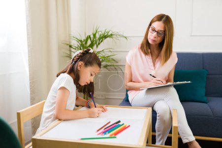 Focused child psychologist observes a little girl during a therapy session to help understand and improve the child's well-being