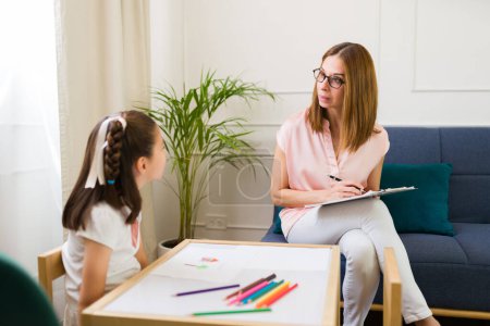 Professional child psychologist engages with a little girl during a therapeutic session in a brightly lit, comfortable office setting