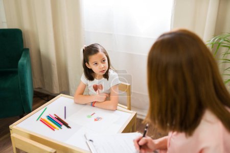 Photo for Cute little girl finishing a drawing as part of a psychological evaluation with a therapist in an office - Royalty Free Image