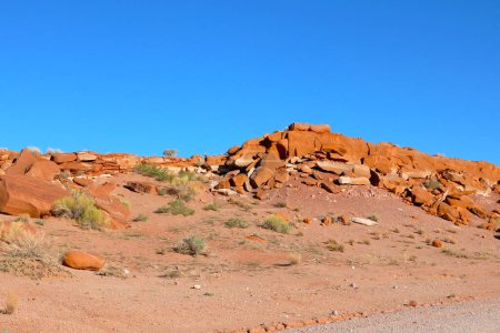 In der trockenen Wüste erhebt sich eine massive Felsformation, die von riesigen Sandflächen und spärlicher Vegetation umgeben ist. Die Felsformation ist verwittert und zerklüftet und trägt die Spuren der Zeit und