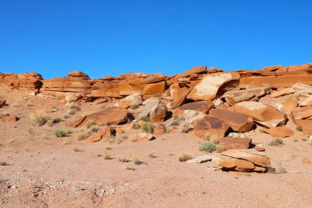 Une grande formation rocheuse domine le paysage désertique stérile, se détachant contre l'étendue vide de sable et de ciel. La formation robuste semble altérée et ancienne, un témoignage de la dure