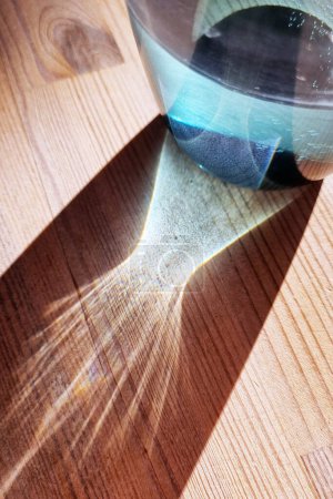 A clear glass filled with water sits on top of a polished wooden table. The light reflects off the glass, creating a simple yet elegant scene.