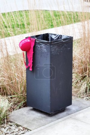 A black trash can is shown with a red hat placed on top of it. The contrast between the black and red colors is striking, drawing attention to the unusual combination of objects.