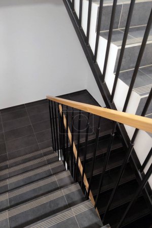 Foto de Un conjunto de escaleras de madera con pasamanos que conducen a un segundo piso en el interior. Las escaleras están iluminadas por la iluminación de arriba, proyectando sombras en los escalones. - Imagen libre de derechos