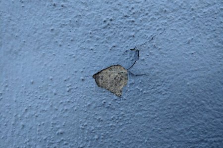 Photo for A crack runs vertically along the side of a blue wall, showing signs of wear and tear. The crack extends from the top to the bottom of the wall, indicating potential structural issues. - Royalty Free Image
