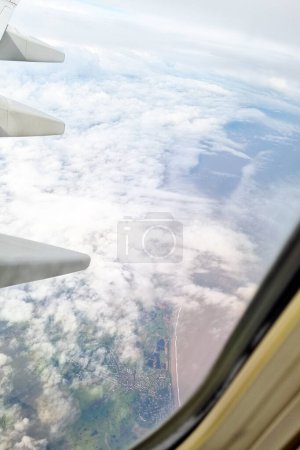 An aerial perspective showing the wing of an airplane, positioned above the clouds during a flight. The wing is visible with its structural components such as flaps, ailerons, and engines.
