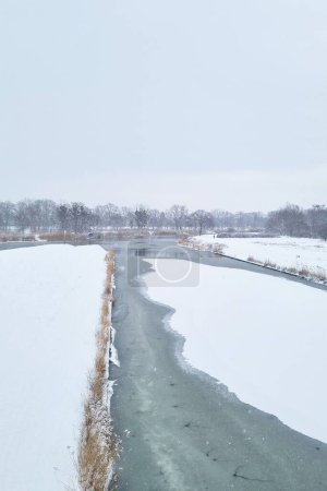 Ein Fluss schlängelt sich durch ein riesiges Feld, das von tiefem Schnee bedeckt ist, und kontrastiert das dunkle Wasser mit der unberührten weißen Landschaft. Die Strömung der Flüsse durchschneidet den Schnee und schafft komplizierte Muster in