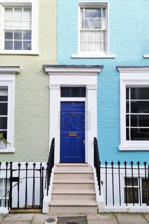 Photo for London, United Kingdom, February 25, 2024: A blue door stands out against a row of vibrant, multi-colored houses. The door is the focal point, contrasting with the colorful homes behind it, creating a striking visual scene. - Royalty Free Image