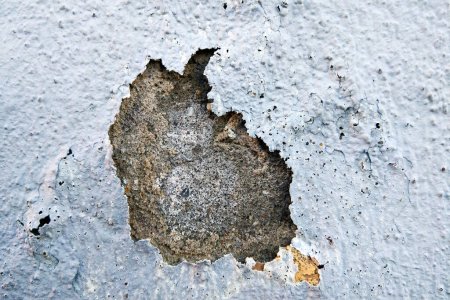 A crack has formed on a concrete wall, revealing a rusted surface underneath. The rust has spread outwards, showing signs of decay and neglect.