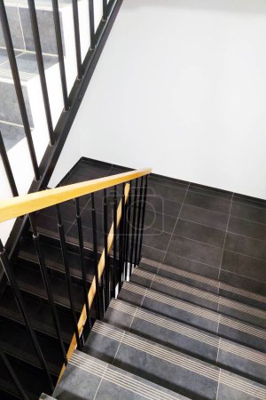 Un escalier noir et blanc avec une main courante jaune vif, offrant contraste et conseils dans un cadre architectural moderne. Les lignes épurées et le design minimaliste créent un impact visuel frappant.