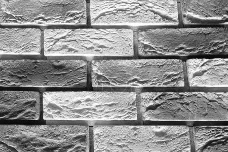 A black and white photograph of a brick wall with a rough texture and visible mortar joints. The bricks are laid in a traditional running bond pattern.
