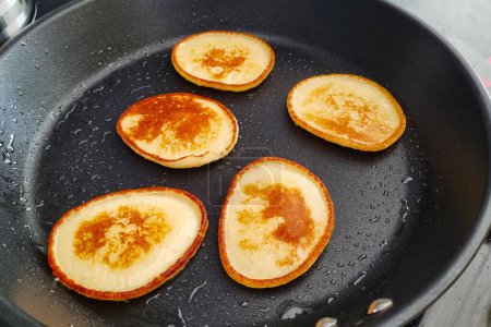 Four Golden Brown Pancakes Cooking on Black Non-stick Pan.
