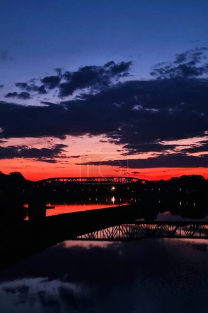 Atemberaubende Sonnenuntergang-Silhouette über Brücke und spiegelndes Wasser.