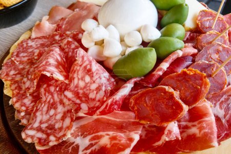 Bandeja de charcutería italiana con una variedad de carnes curadas, incluyendo salami, prosciutto y chorizo, acompañados de mozzarella fresca y aceitunas. perfecto para comer gourmet, entretener, o como aperitivo en una reunión.