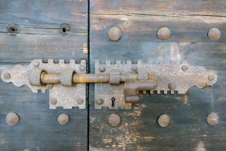 Rustikale alte Holztür mit einem alten Eisenschloss und Riegelmechanismus. Diese Nahaufnahme hebt komplizierte Metallarbeiten und gealterte Texturen hervor, ideal für Architekturstudien, historische Referenzen oder Design-Inspirationen.