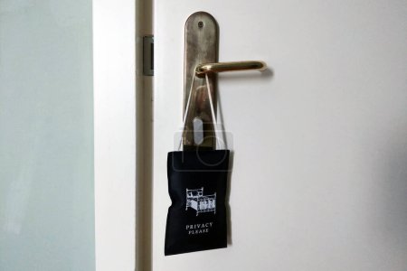 Privacy please door hanger hängen an einer metallischen Türklinke einer weißen Tür, die oft in Hotels verwendet wird, um den Hausherrn und das Personal über das Bedürfnis eines Gastes nach Privatsphäre zu informieren. betont Komfort, Sicherheit und unaufdringlichen Service im Gastgewerbe.