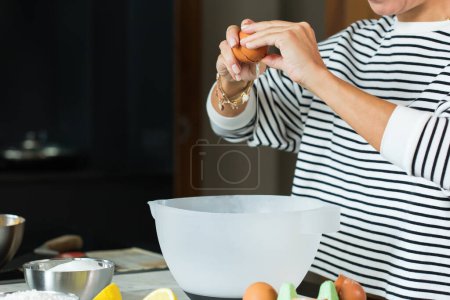 Téléchargez les photos : Woman breaking eggs while cooking apple pie in the modern kitchen - en image libre de droit