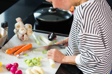 Téléchargez les photos : Woman slicing vegetables while cooking stew. Close up of woman hands cutting vegetables on a cutting board at the modern kitchen - en image libre de droit