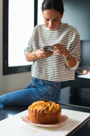 Photo for Woman making a photo for a social media on her phone while cooking apple pie in the modern kitchen - Royalty Free Image