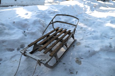 Téléchargez les photos : Old children's sleds are standing in the snow on a winter day. Old metal sleigh in the snow. A product for winter skiing. Children's sled with rope, on a white background. . - en image libre de droit