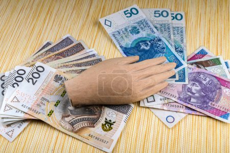 Foto de Hay muchas copias de papel moneda polaco con la mano de madera de un ídolo en ellos.El amor excesivo de dinero.El concepto de la crisis financiera. - Imagen libre de derechos