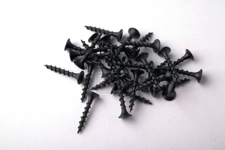 Black self tapping metal, screw white background.Black metal self-tapping screws on wood on a white table. Long black screws on drywall.