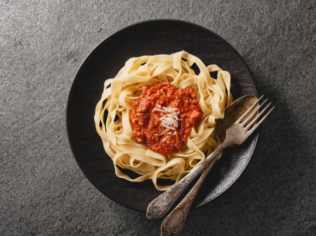 Close-up of a plate of freshly tagliatelle pasta with BOLOGNESE SAUCE prepared according to a classic recipe. Gray background from natural stone. Top view.