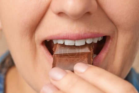 Téléchargez les photos : Gros plan de la bouche d'une femme blanche mangeant du chocolat poreux. Vue de face depuis un angle bas. - en image libre de droit