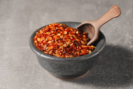 Dried chili pepper flakes in a gray bowl on a gray background. Front view.