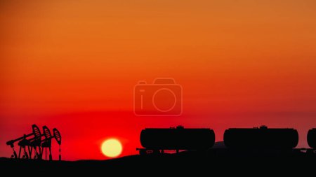 Téléchargez les photos : Silhouette industrielle sur fond de coucher de soleil lumineux avec pompes à huile et réservoirs ferroviaires. - en image libre de droit