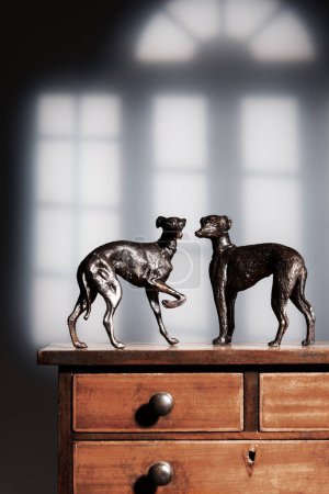 Antique bronze greyhound dogs standing on top of mahogany cabinet
