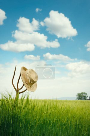 Foto de Sombrero de paja sentado en la parte superior de tenedor de heno en el campo de verano - Imagen libre de derechos