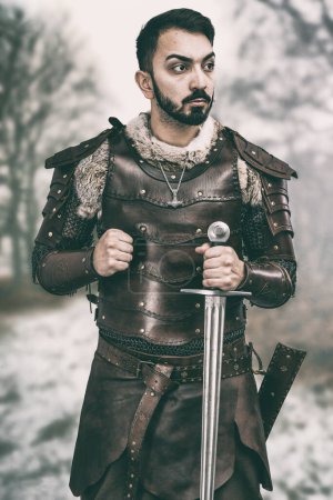 Téléchargez les photos : Homme en costume médiéval en cuir fait main tenant son épée - en image libre de droit
