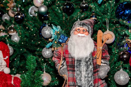 Téléchargez les photos : Poupée Santa Clause décorée devant le sapin de Noël avec des jouets ornementaux colorés lors du festival de Noël dans le monde entier - en image libre de droit