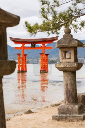 O-torii ( Grand Torii Gate ) stands in Miyajima island bay beach at low tide. Itsukushima Shrine stone lanterns and pine tree. Hiroshima, Japan.
