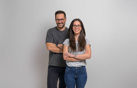 Photo for Portrait of smiling young couple wearing eyeglasses and casuals standing confidently against background. Joyful handsome man and beautiful woman posing with arms crossed - Royalty Free Image